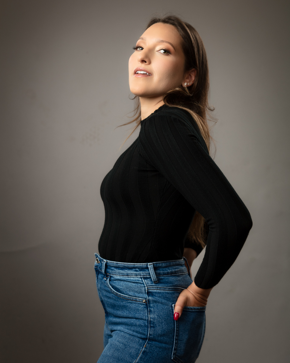Woman in black top and jeans posing over grey background