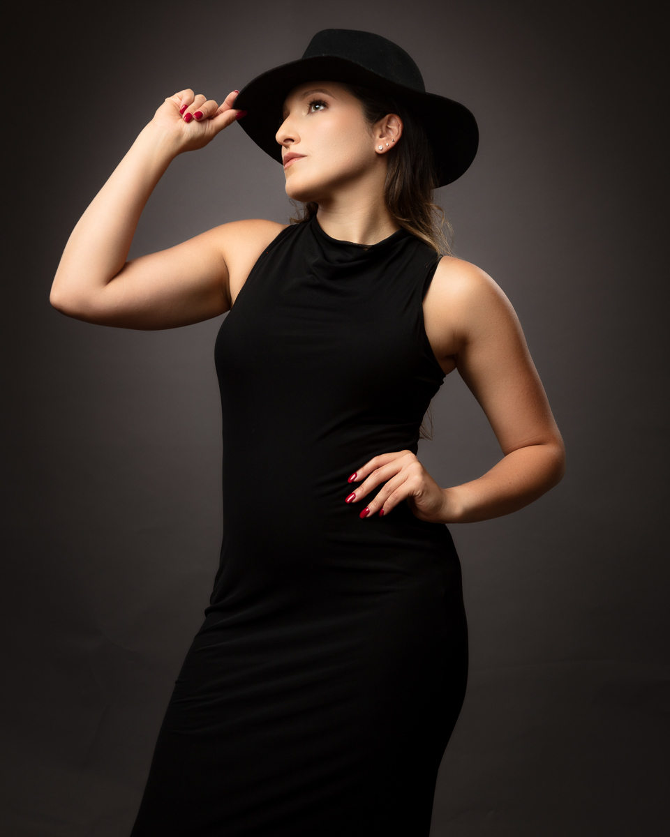 Woman wearing black hat and dress against grey background