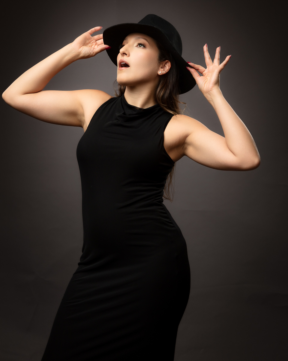 Woman in black outfit and cap posing expressively upward