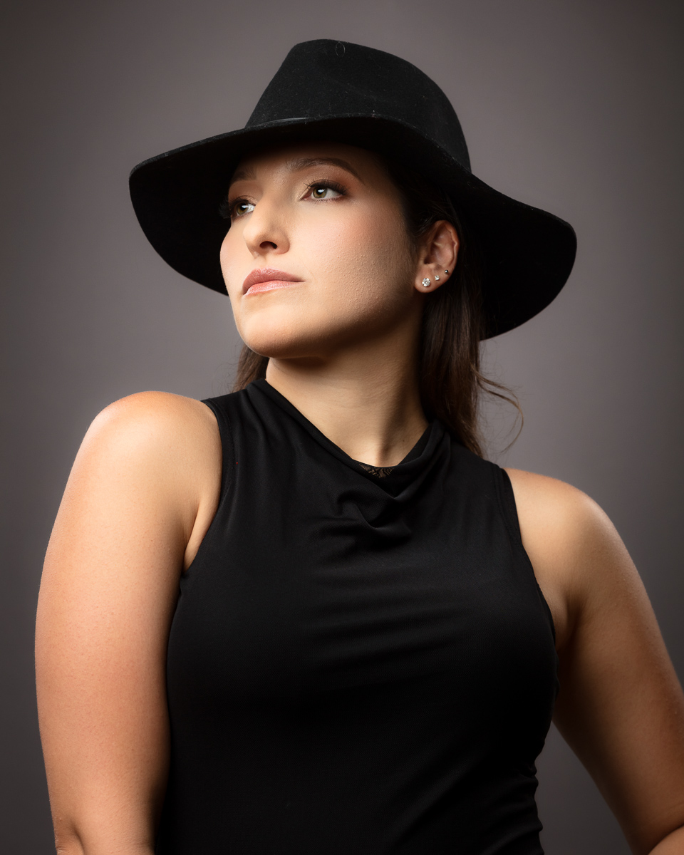 Woman wearing black hat and sleeveless top looking upward