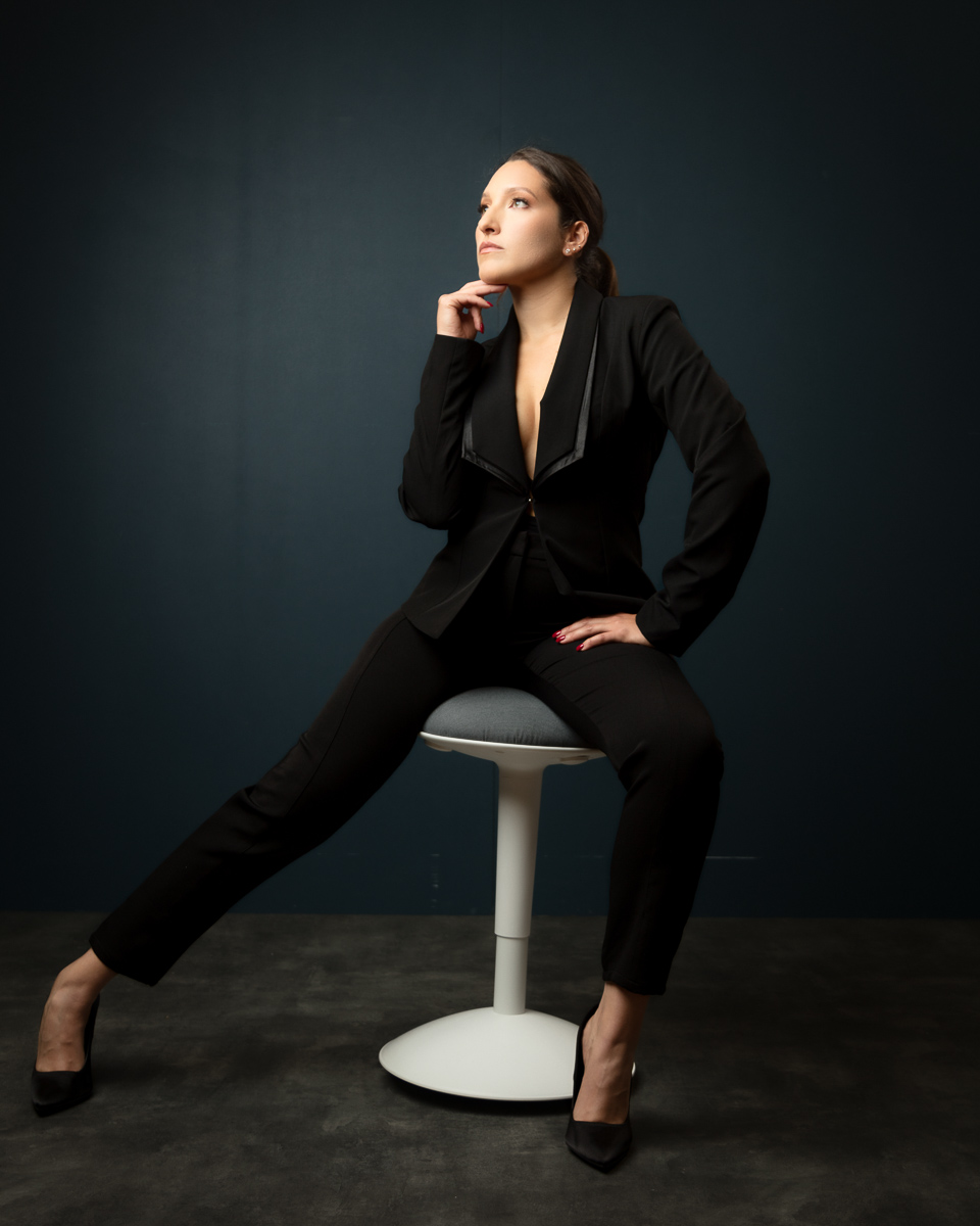 Professional woman in black business suit sitting thoughtfully on stool