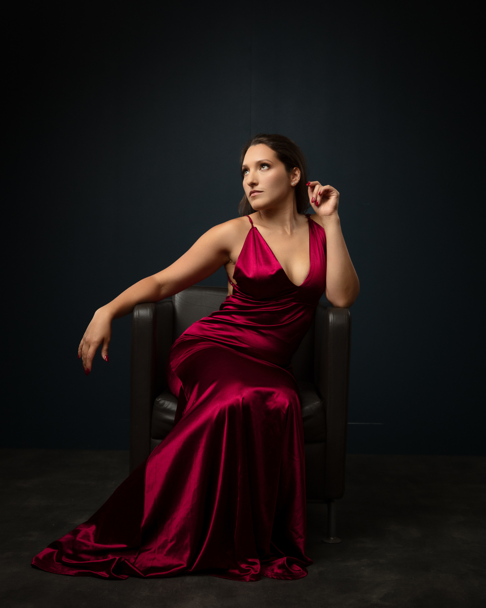 Woman in red evening gown seated on black armchair