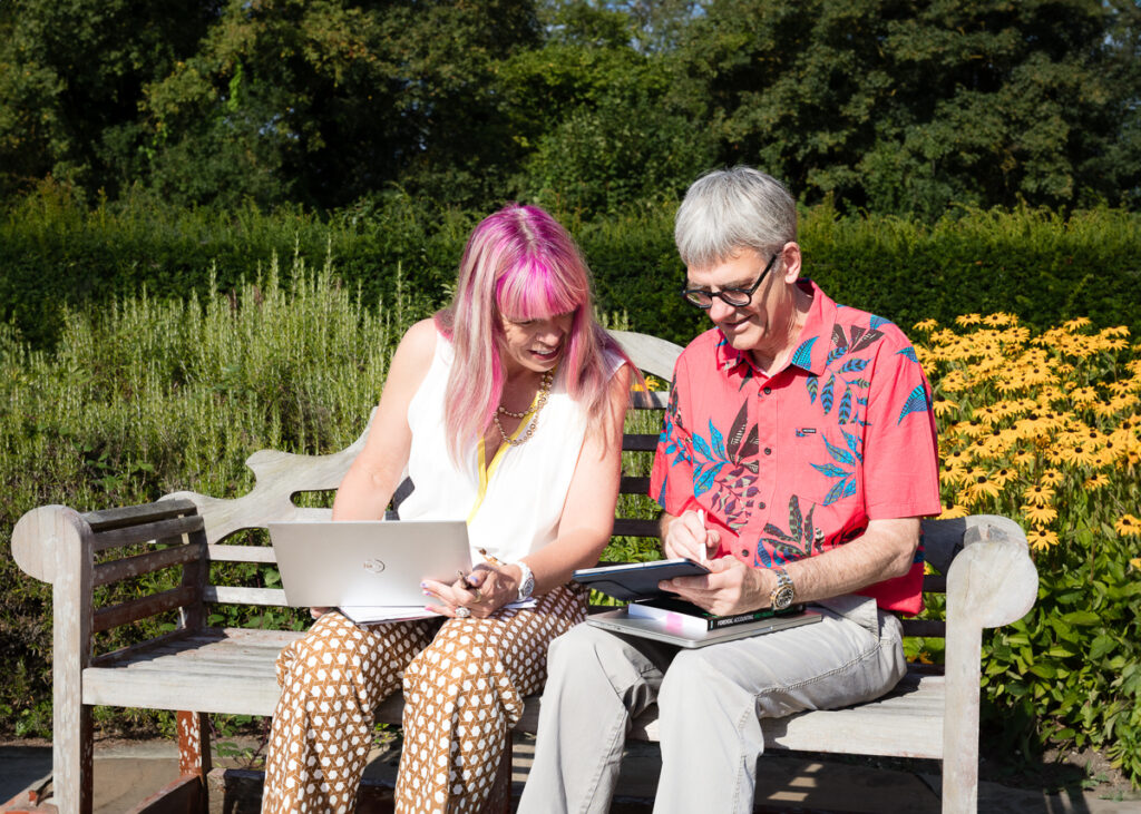 Two people using laptops on a garden bench.