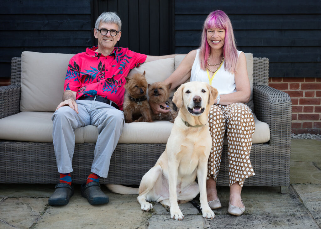 Couple sitting on sofa with three dogs.