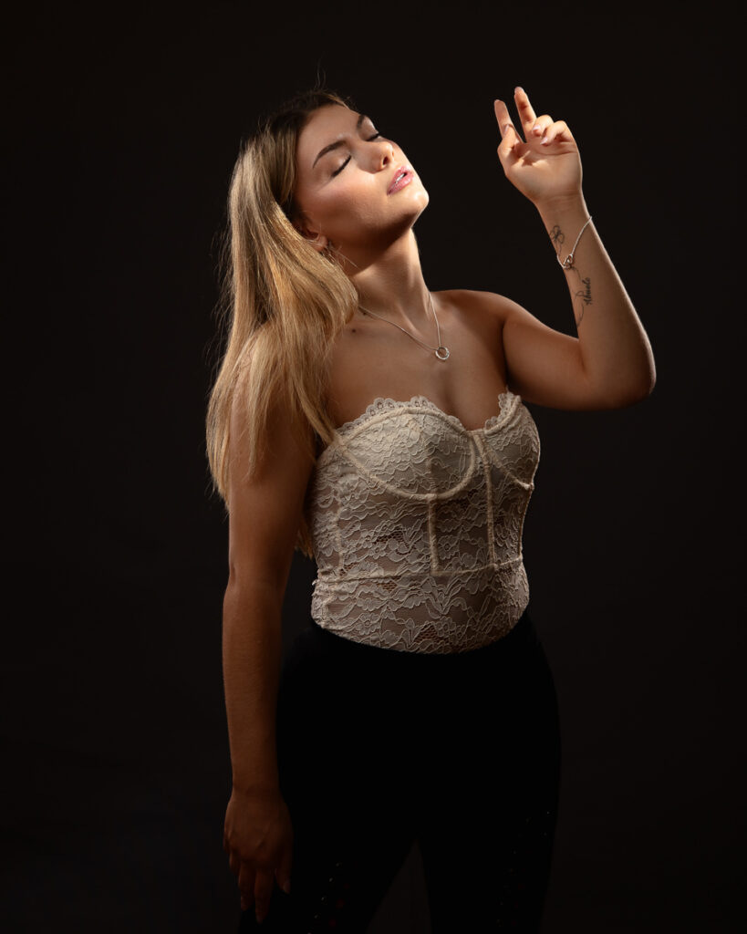 Woman in lace top posing against dark background.