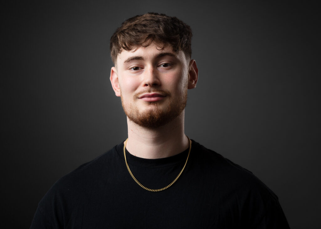 Man in black shirt with chain, smiling.