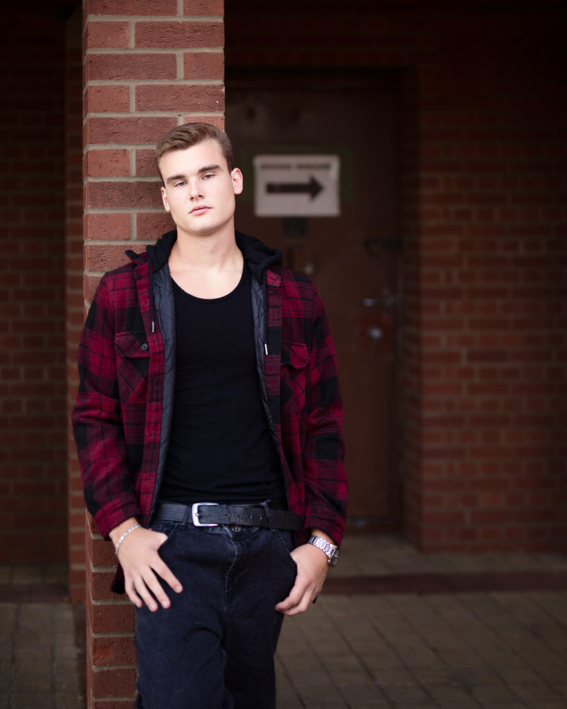 Man leaning on brick wall, serious expression.