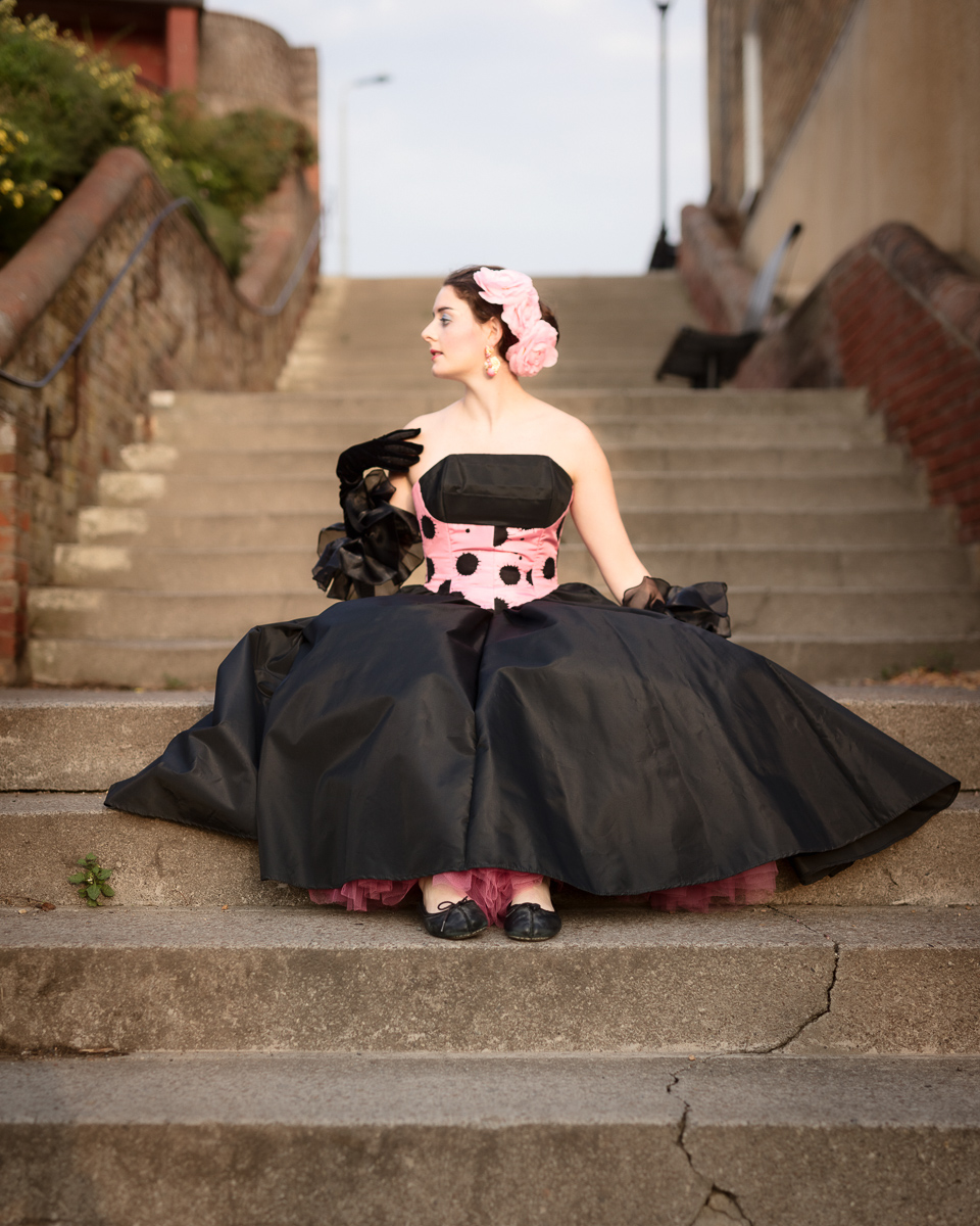 Woman in Victorian dress sitting on staircase.