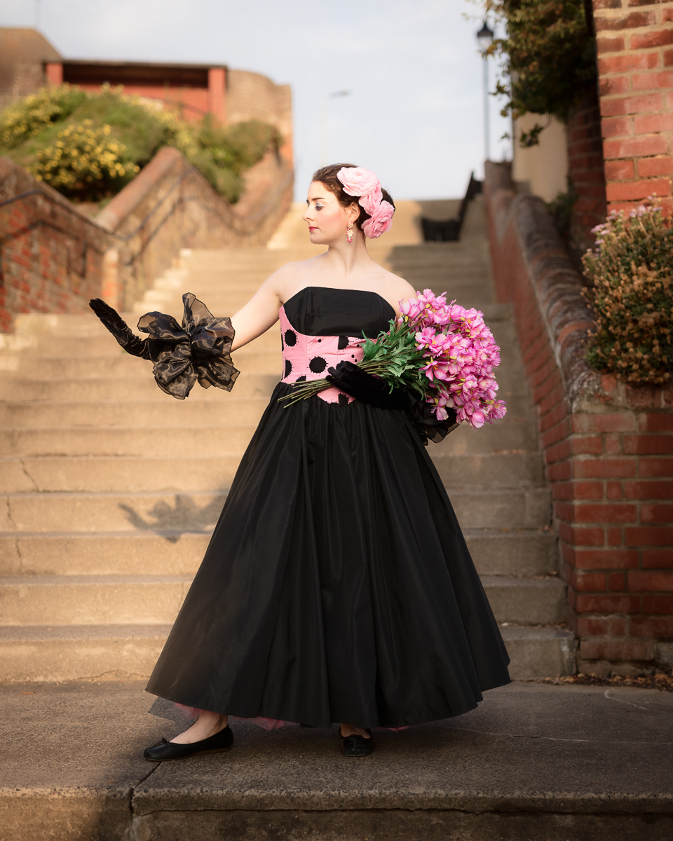 Woman in vintage dress holding pink flowers on steps.