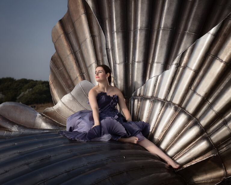 Woman in dress on metal shell sculpture.