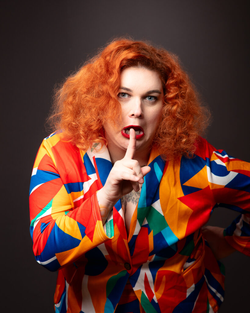 Person with finger raised to lips, colourful jacket