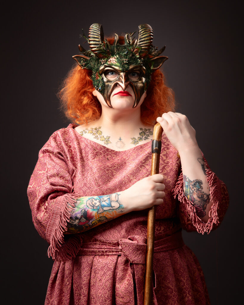 Person in ornate mask and robe holding staff.