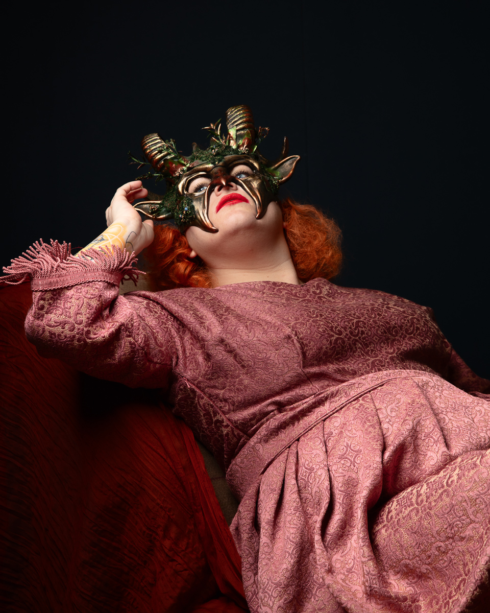 Woman in ornate mask and pink gown reclining