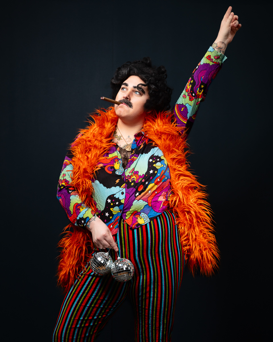 Flamboyant man in vibrant orange fur coat holding disco balls