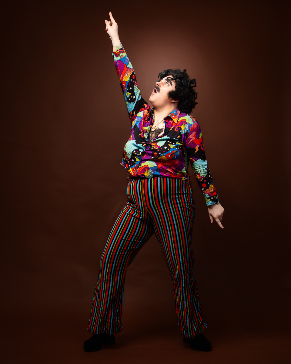Person in colourful 70s disco outfit pointing upward.