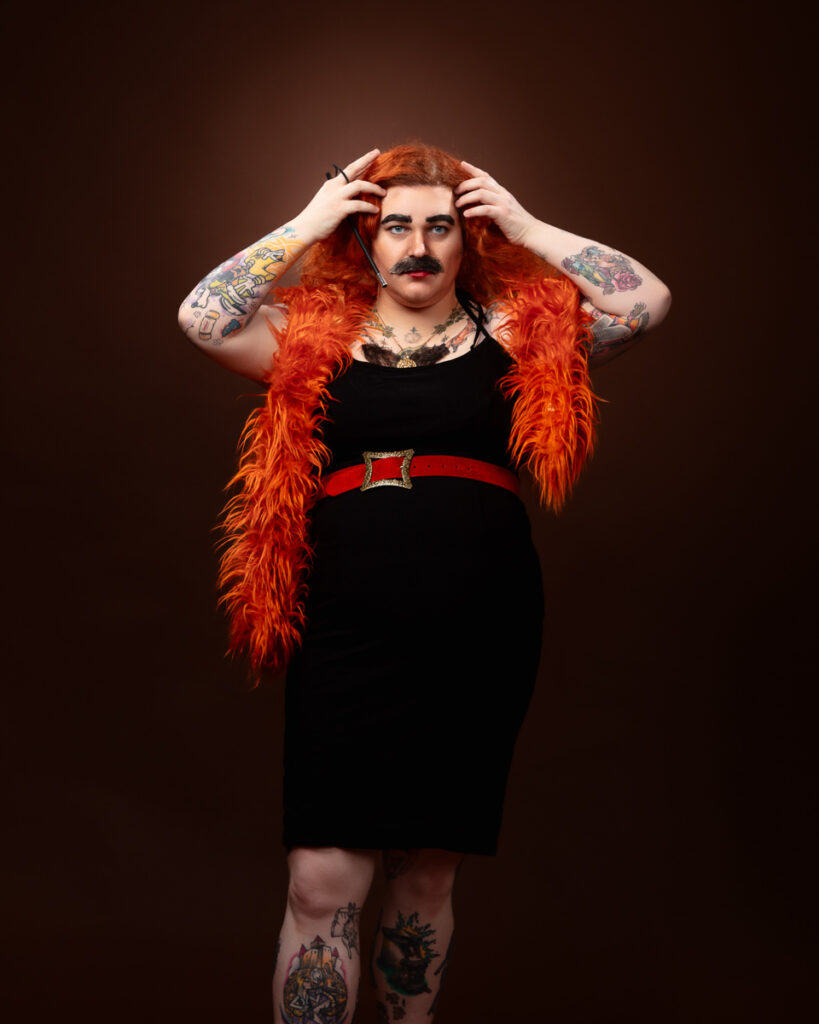 Person with red wig, tattoos, and orange feather vest.