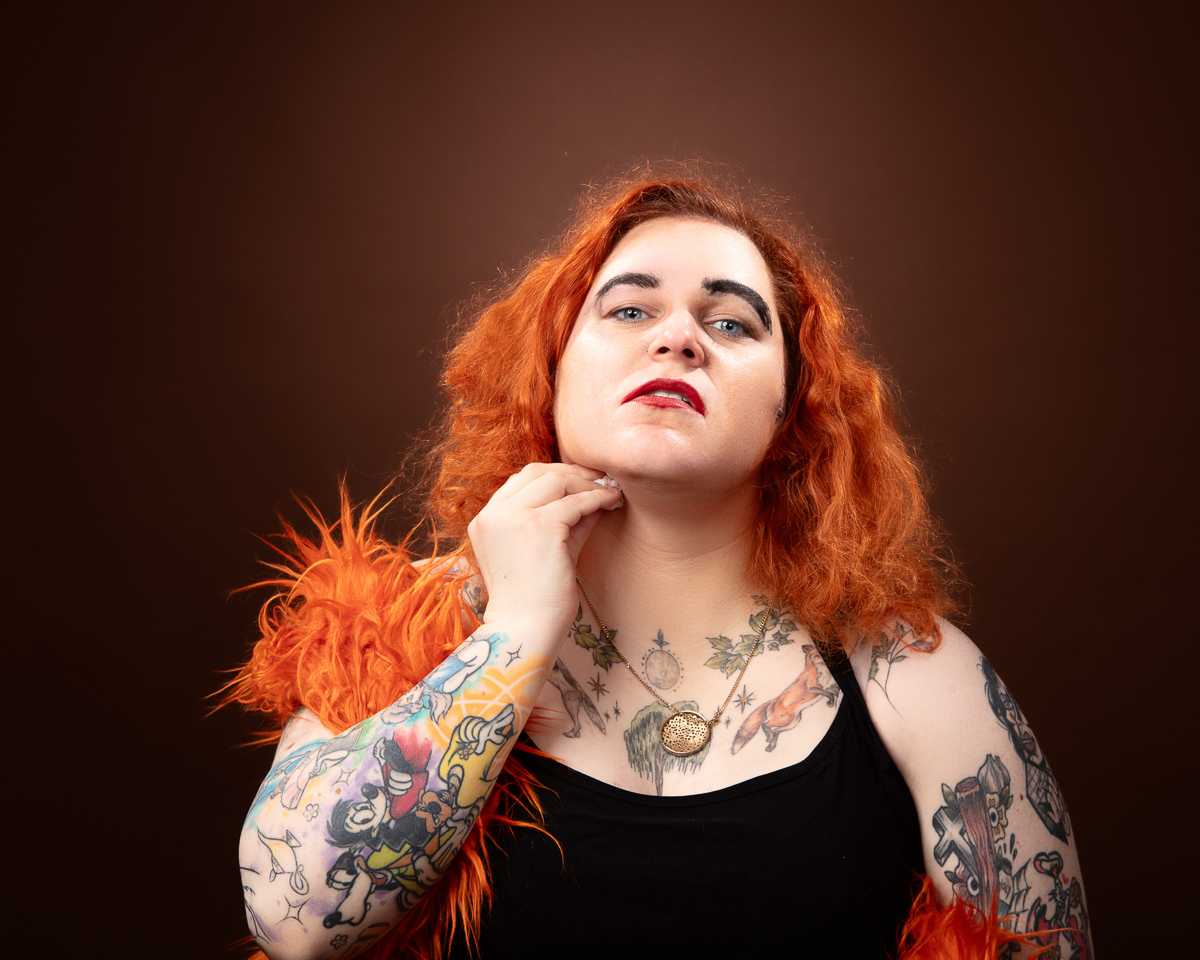 Woman with red hair and tattoos posing confidently.