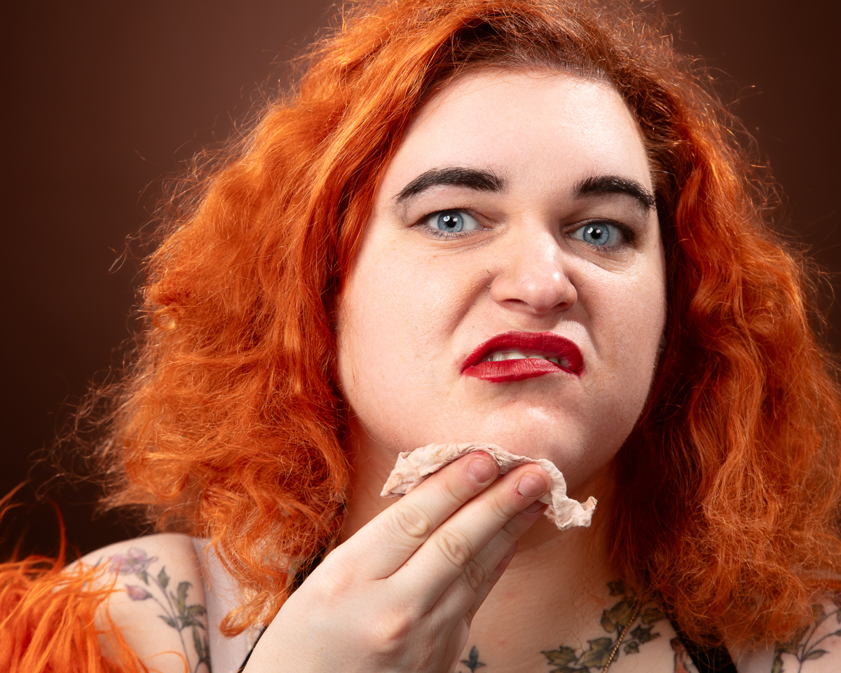 Red-haired person wiping face with tissue.