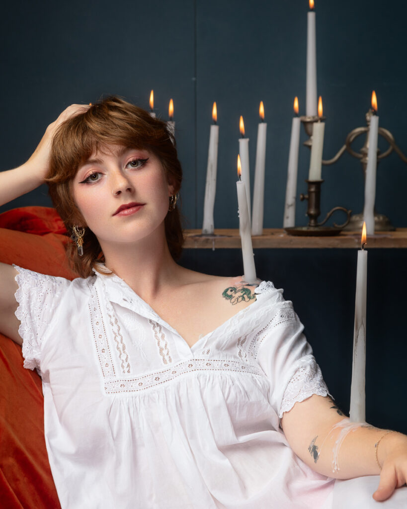 Person in white dress surrounded by lit candles.