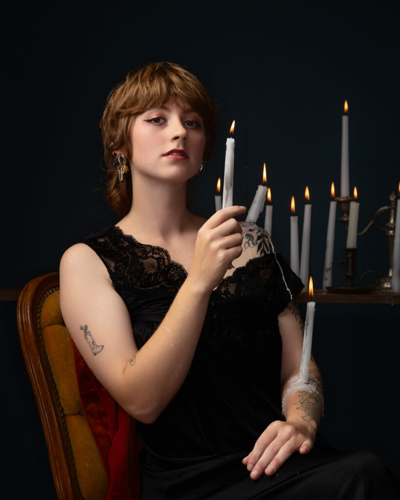 Person holding lit candle with tattoos visible.