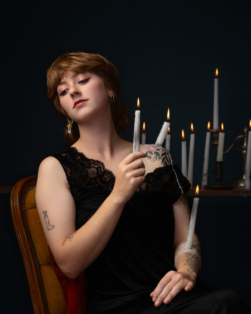 Tattooed person holding lit candles in dim lighting.