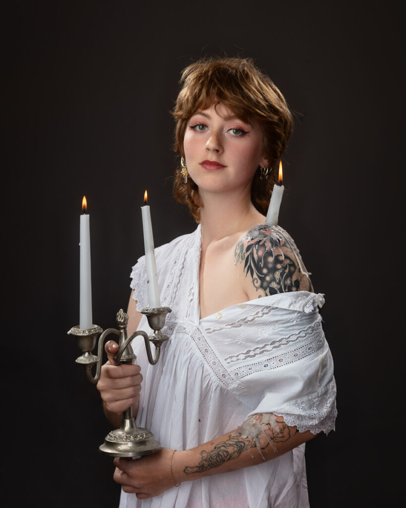 Tattooed woman holding candlestick with lit candles.