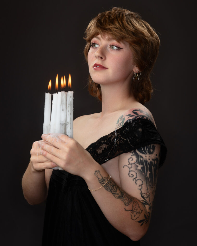 Tattooed woman holding candles, dark backdrop.