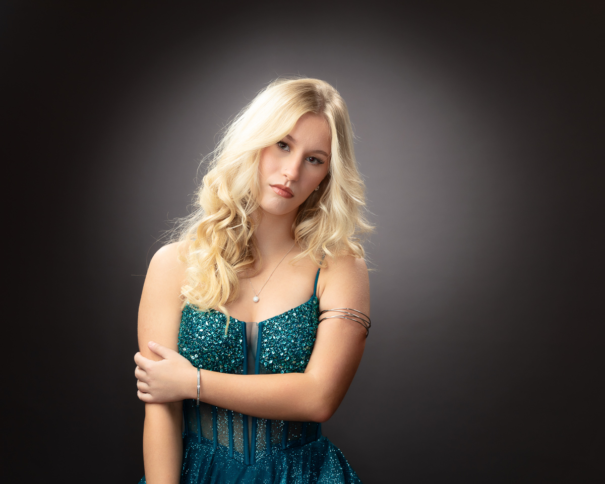 Blonde woman in sparkling teal dress, posing elegantly.