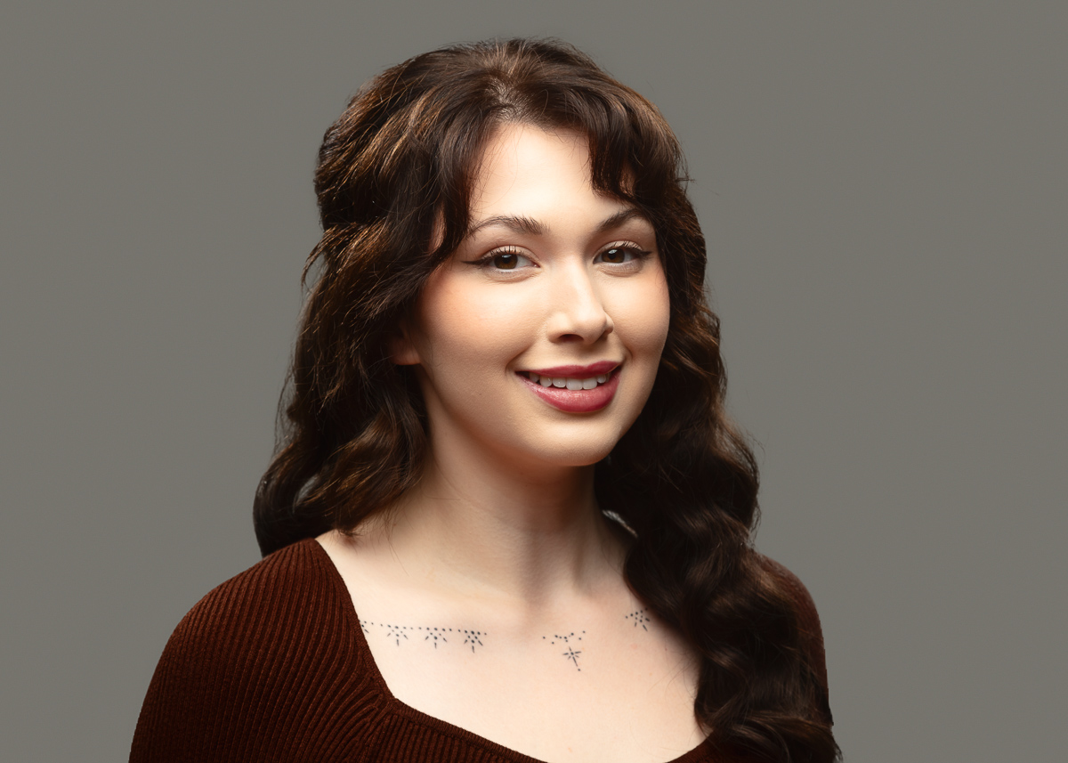 Woman with dark wavy hair smiling against grey background