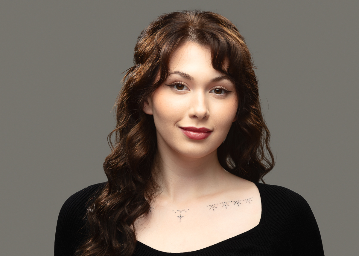 Smiling woman with wavy brown hair and tattoo.