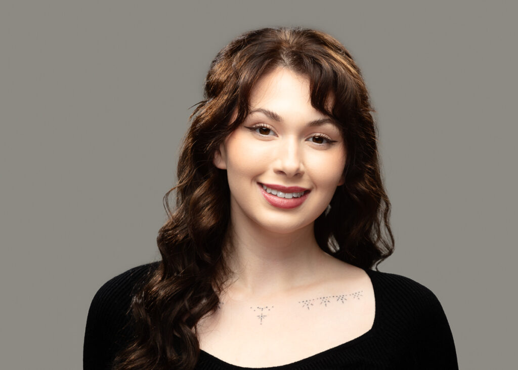 Smiling person with curly hair and shoulder tattoos.