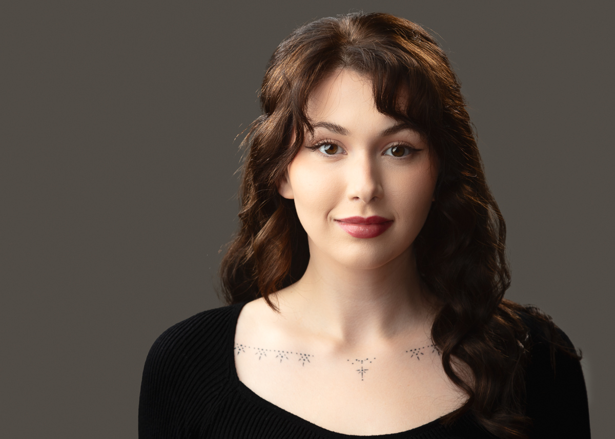 Woman with dark hair and a tattooed neckline.