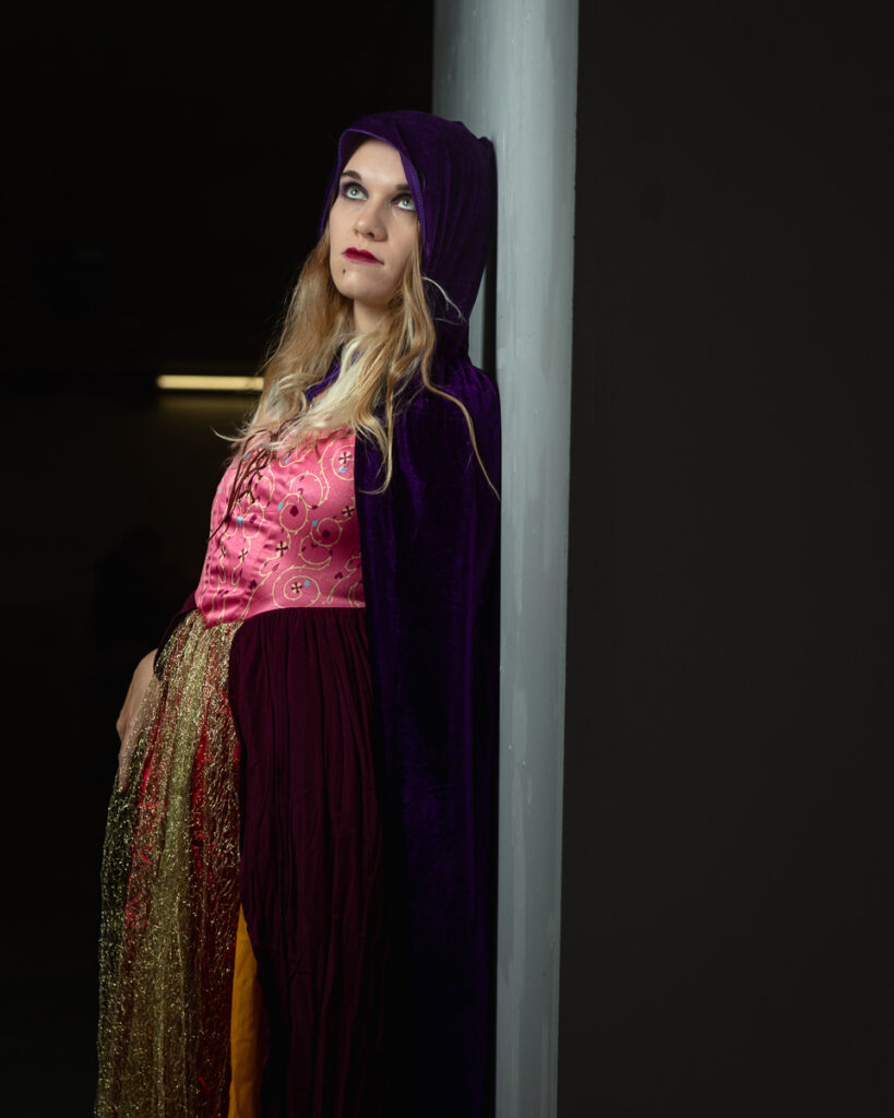 Woman in vibrant costume with purple hooded cloak.