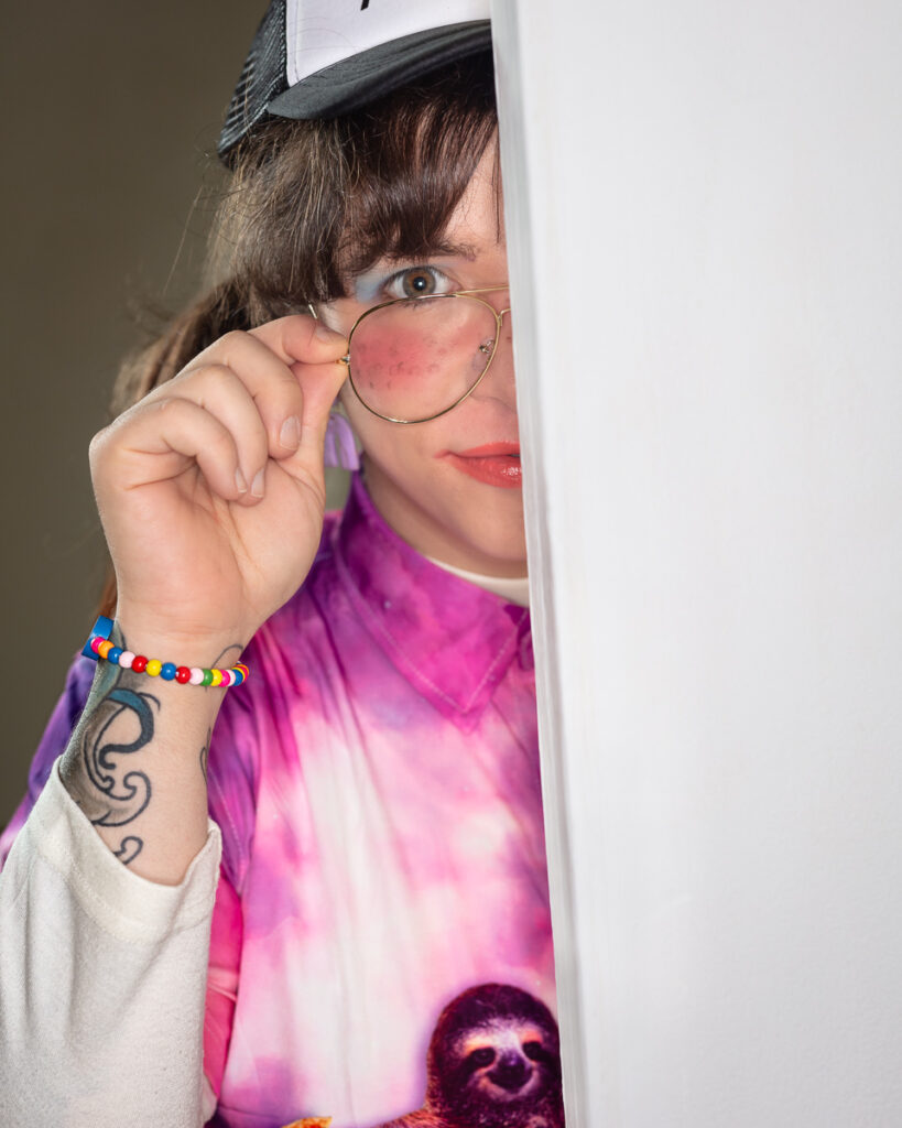 Person wearing cap and rose-tinted glasses peeking around corner