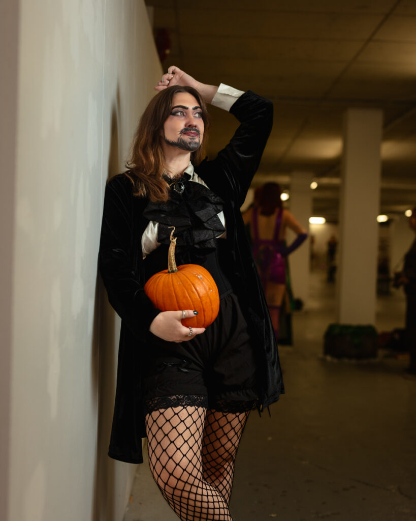Person in gothic Halloween costume holding orange pumpkin indoors