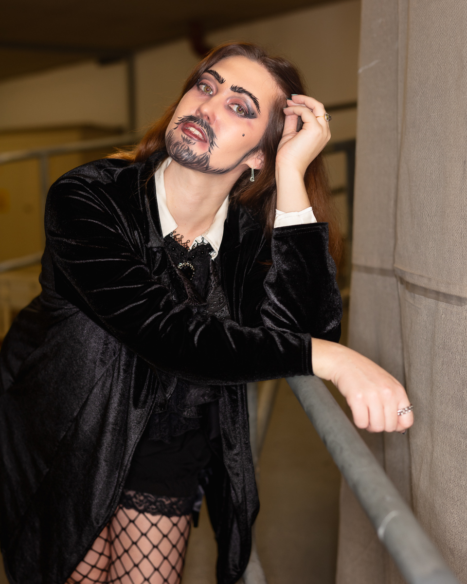 Person with artistic facial hair makeup wearing black velvet jacket
