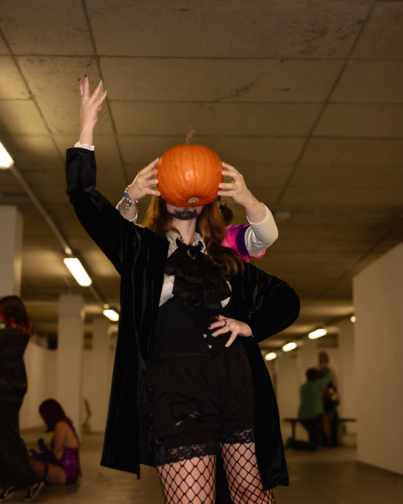 Person in black outfit holding orange pumpkin on head