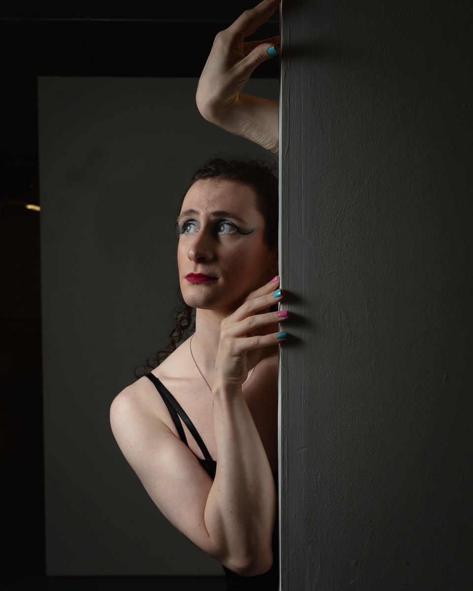 Woman peeking cautiously around dark wooden doorframe