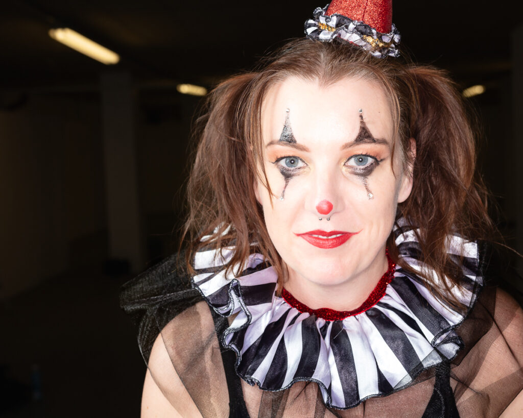 Woman in elaborate clown costume with red nose and makeup