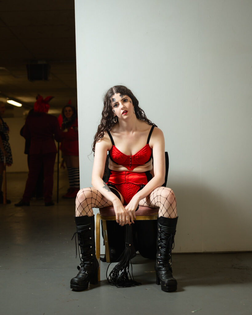 Woman in red corset and fishnet stockings seated on chair