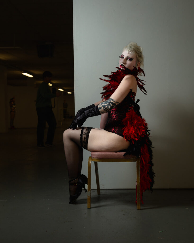 Person in bold red feathered costume striking dramatic pose on chair