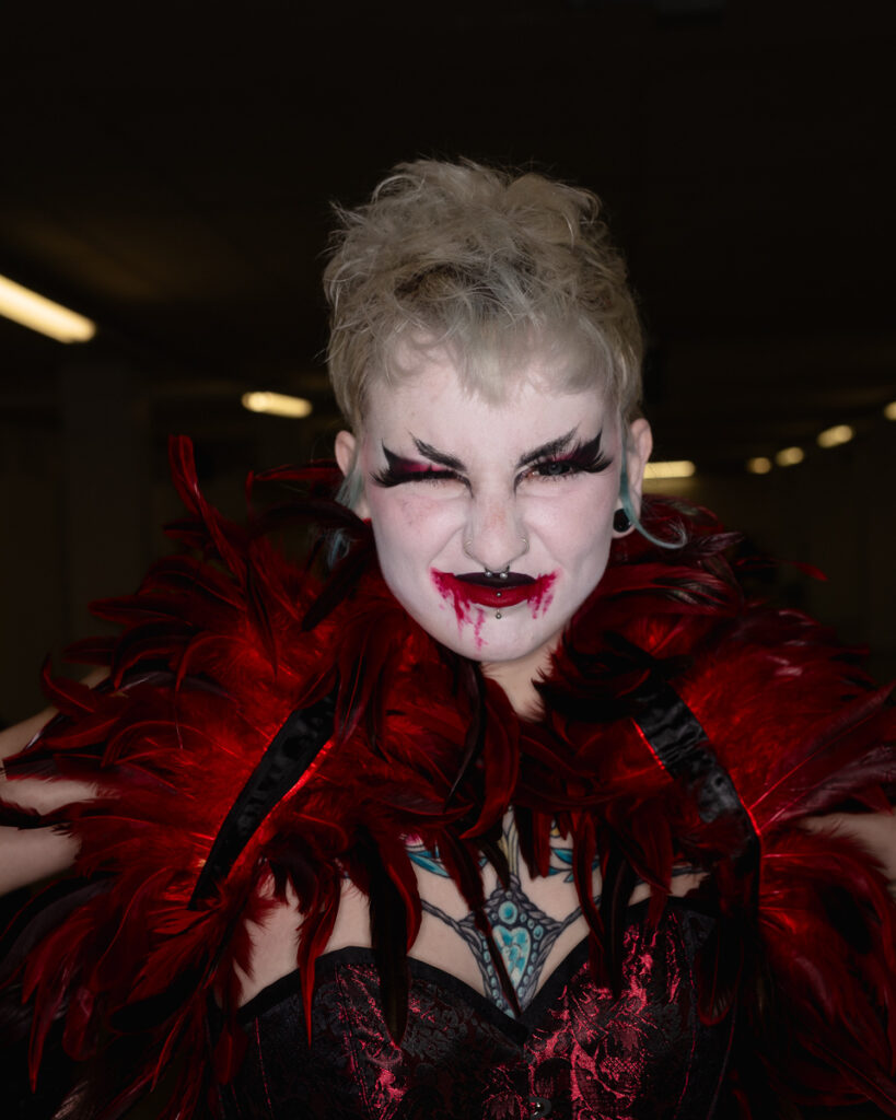 Person in theatrical vampire makeup and red feathered costume
