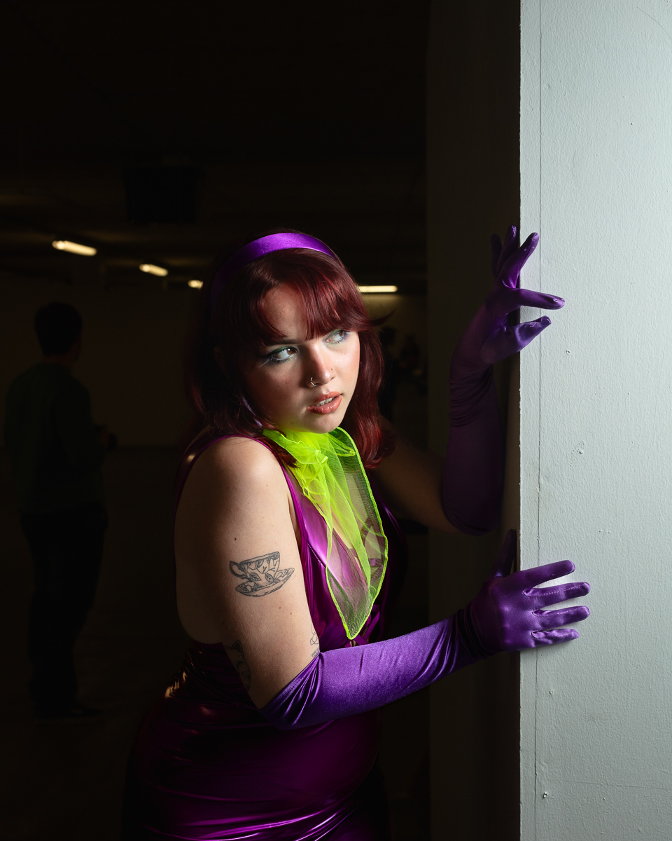 Woman in purple outfit with neon accents posing against wall