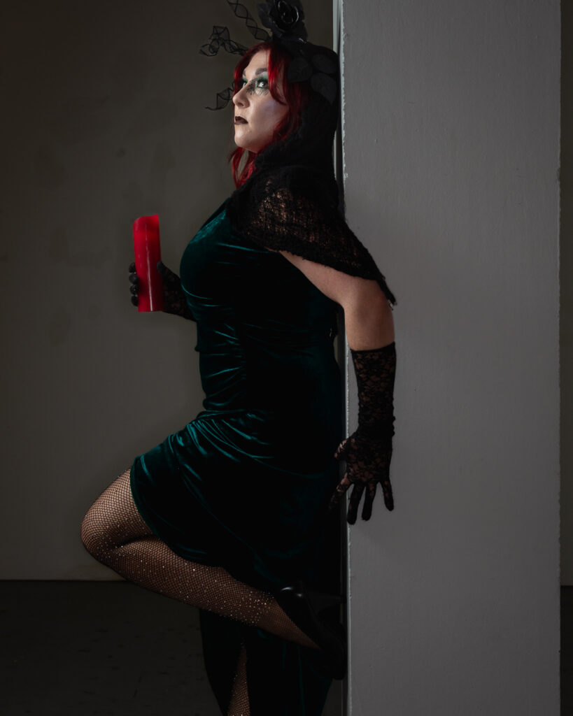Woman with red hair in gothic teal velvet dress holding candle