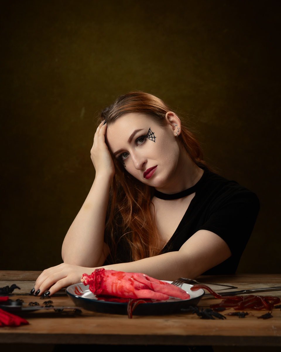 Woman with Halloween makeup, severed hand prop on table.