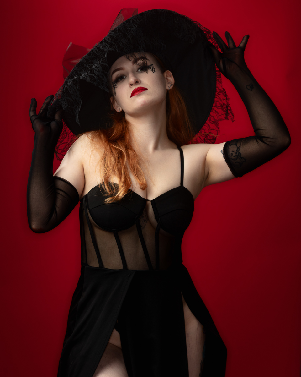 Woman in black corset and wide-brimmed hat against red background