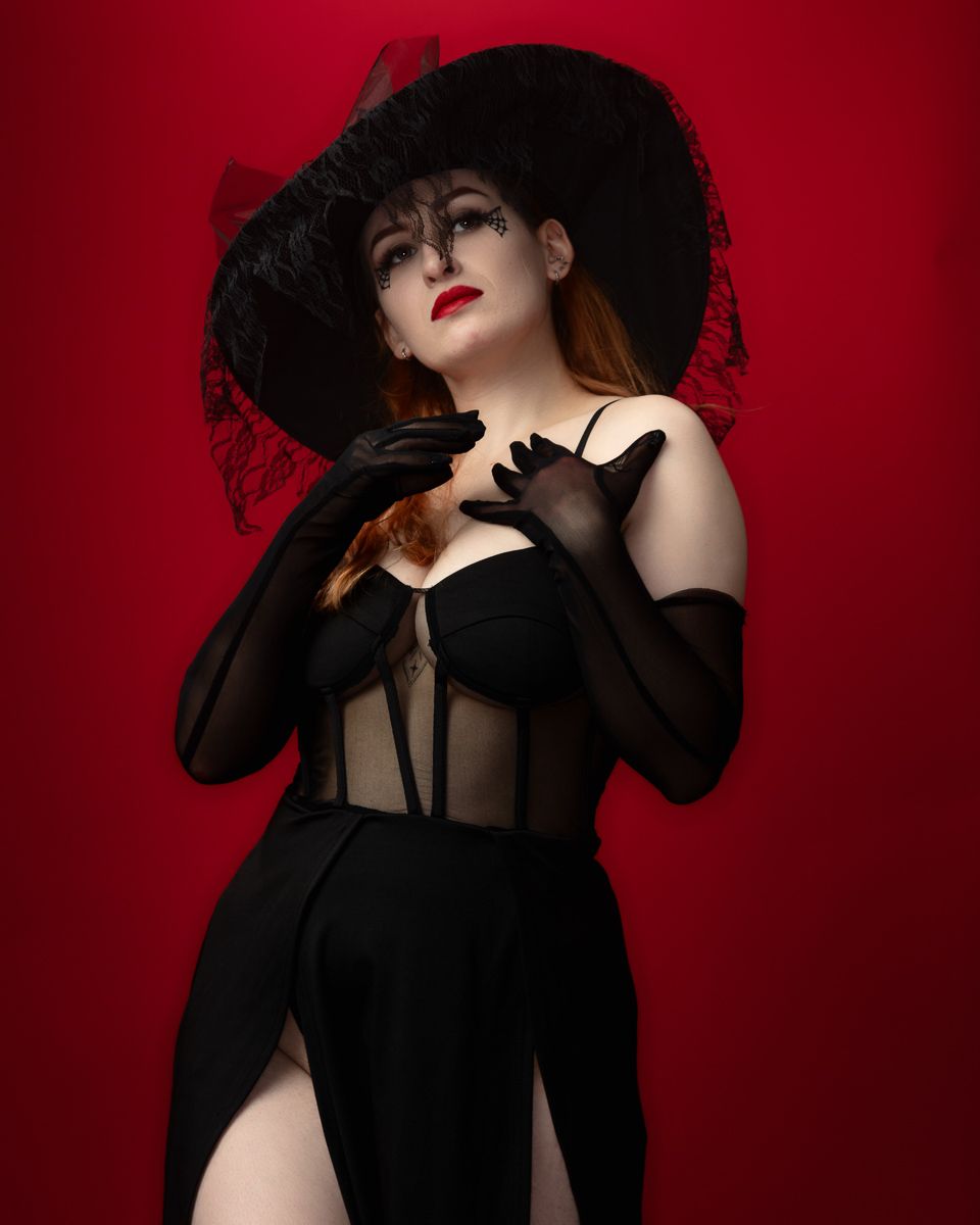 Woman in black dress and wide-brimmed hat against red background