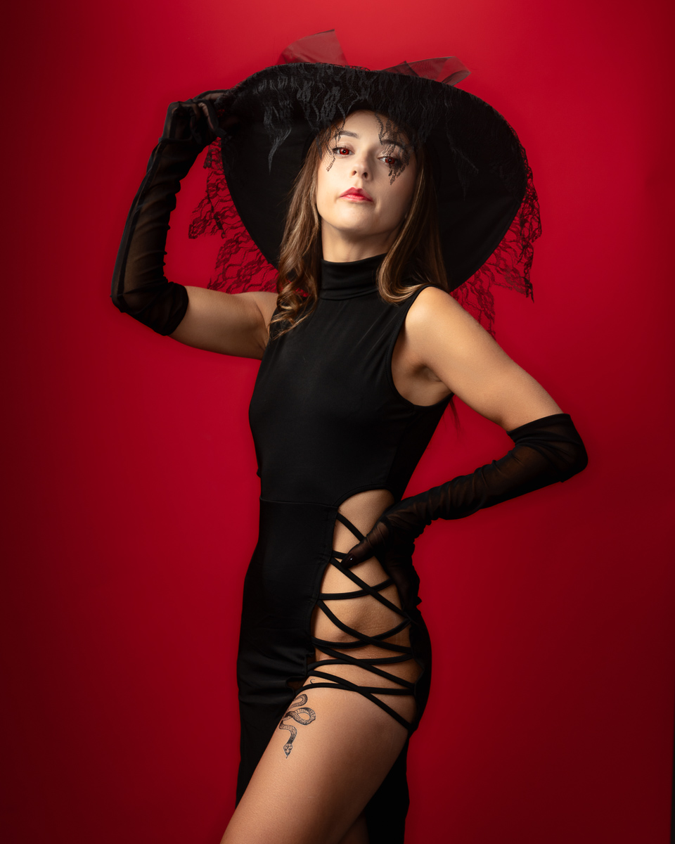 Woman in black dress wearing wide-brimmed hat against red background