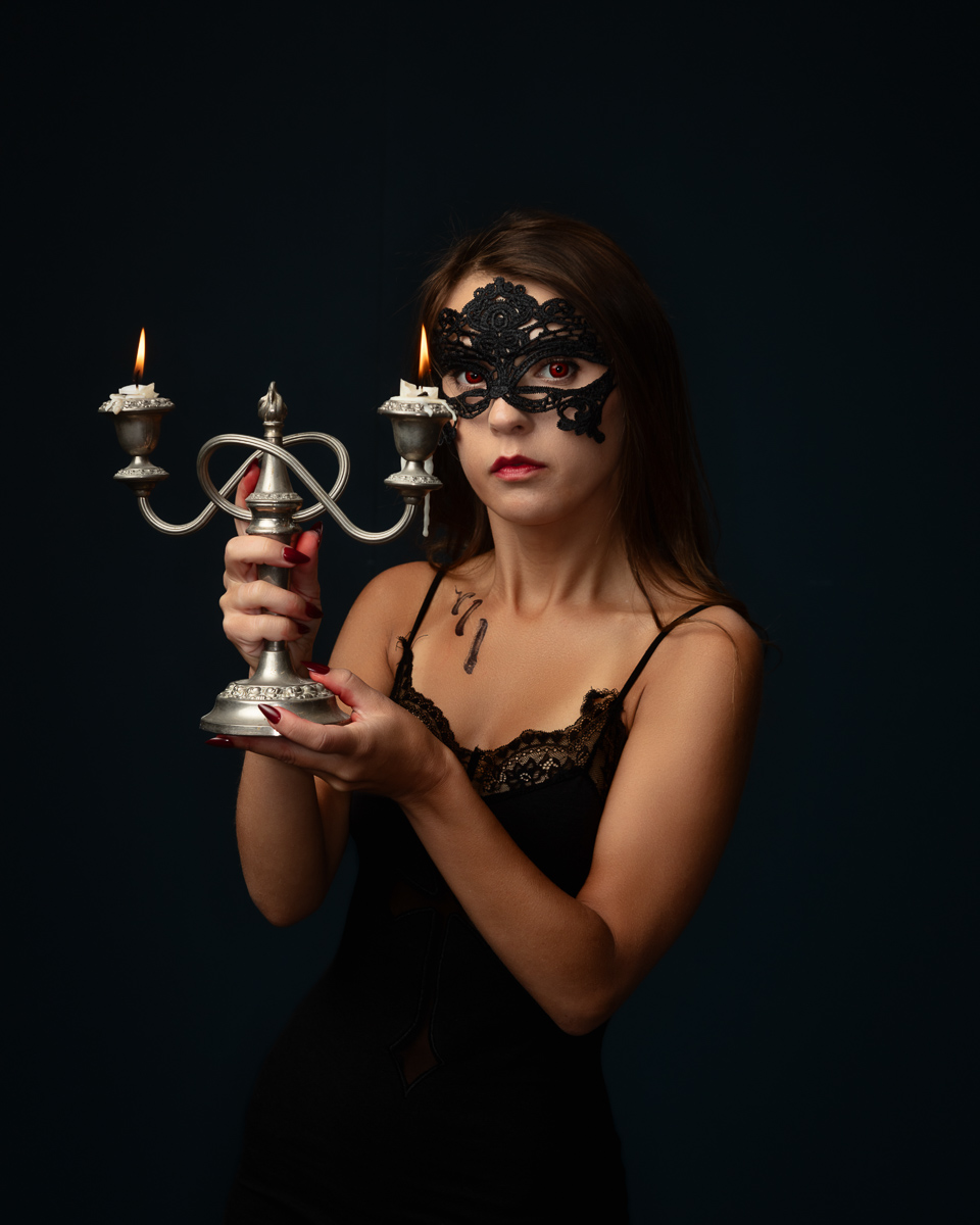 Woman wearing black lace mask holding ornate silver candelabra