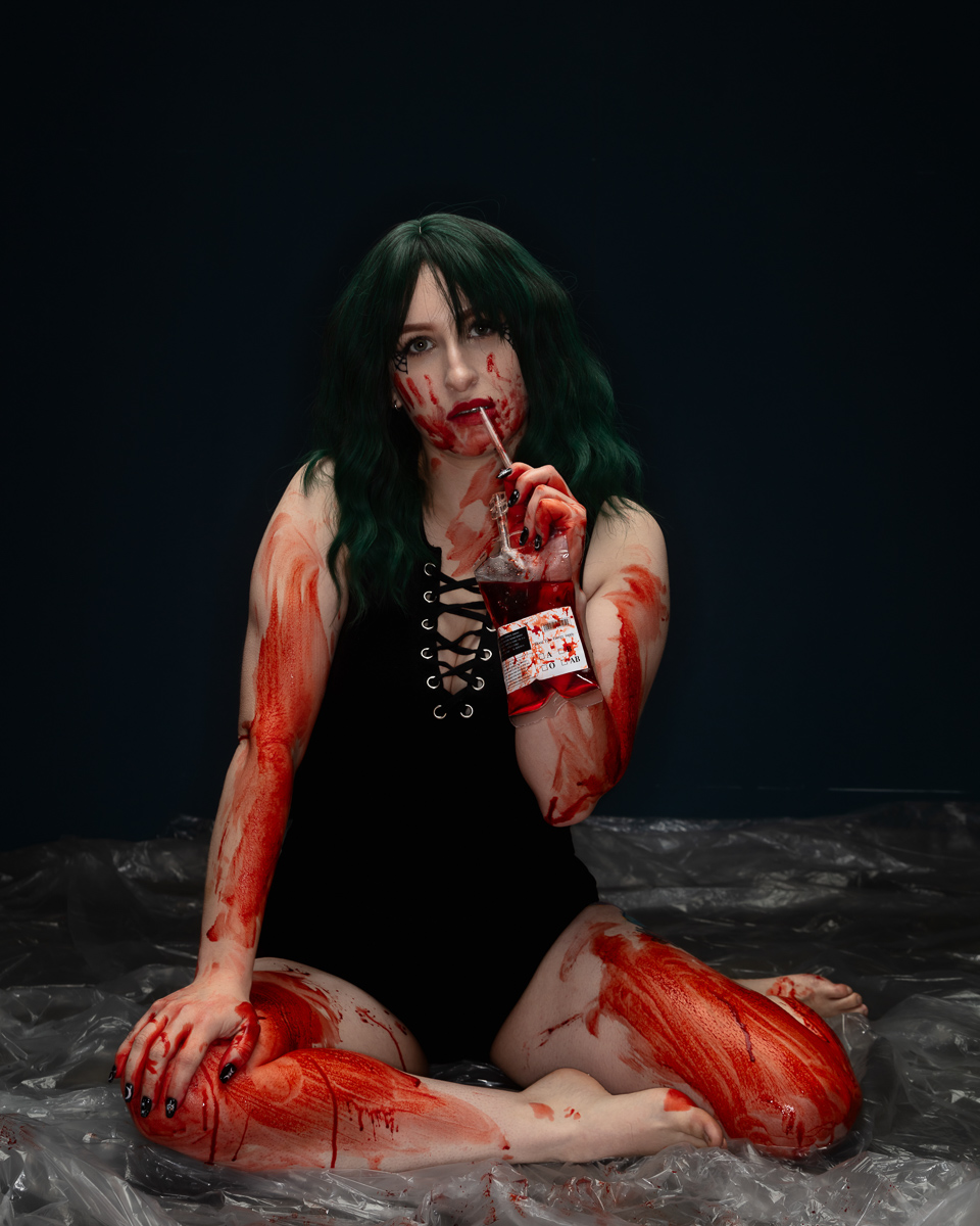 Person with dark hair in gothic costume with red paint effects